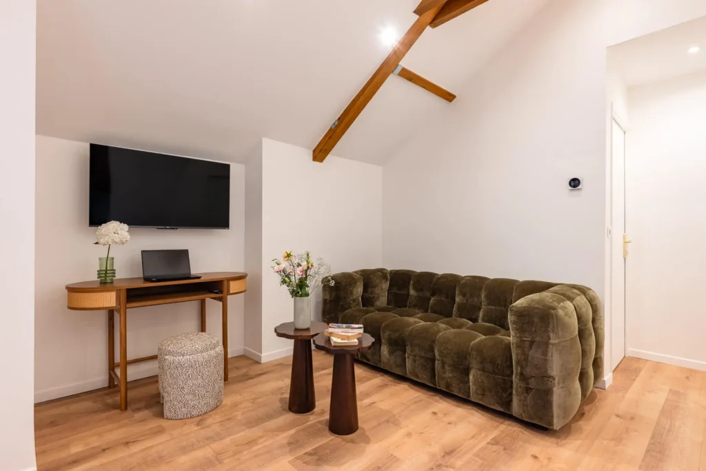 Salon avec canapé en velours, bureau et TV murale dans un appartement 1 chambre